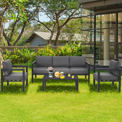 Outdoor patio set with gray sofa and chairs on a grassy area.