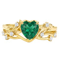Yellow gold ring with a heart-cut emerald centerpiece and diamond accents on an ornate band.